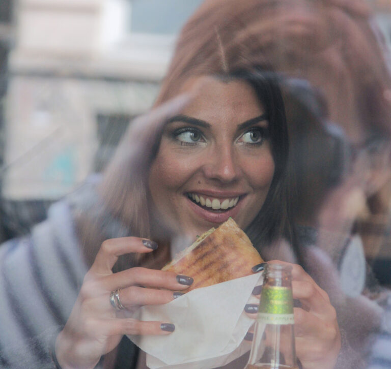 e lachende Frau sitzt mit einem Sandwich in der Hand in einem Café.