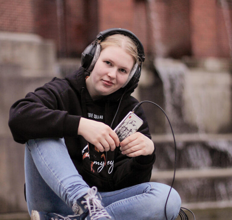 Eine blonde Frau sitzt mit Kopfhörern und einem iPod in der Hand vor dem Planetarium im Hamburger Stadtpark.